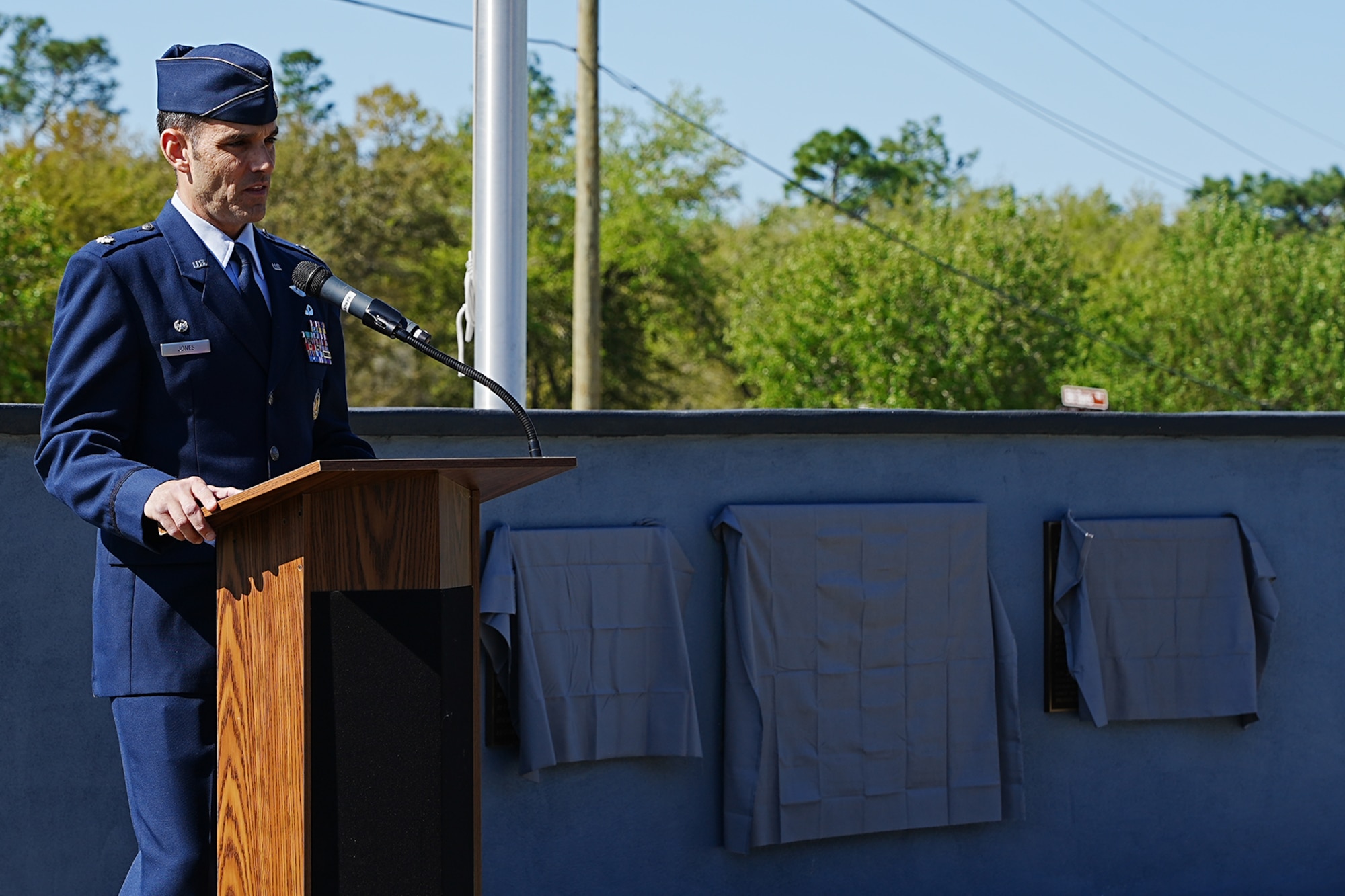 A keynote speaker talks at the podium outside for a memorial dedication.
