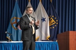 Man in a suit stands with a microphone in his hand