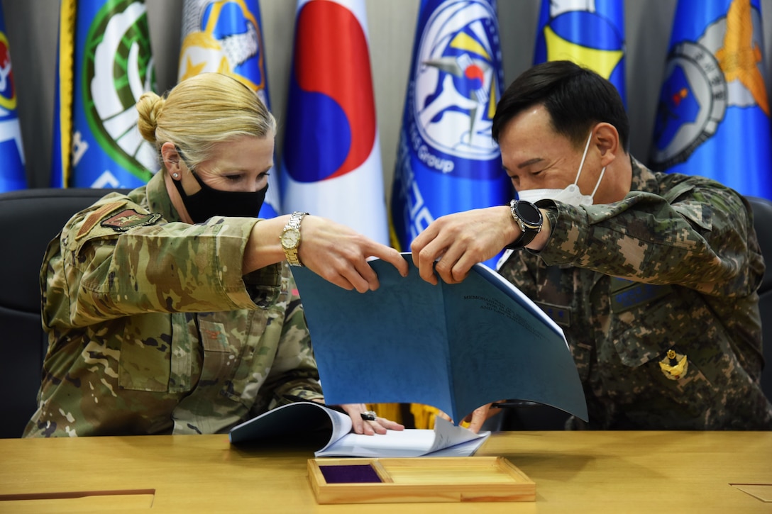 An American officer and an ROK officer both smile while holding and looking at a book.