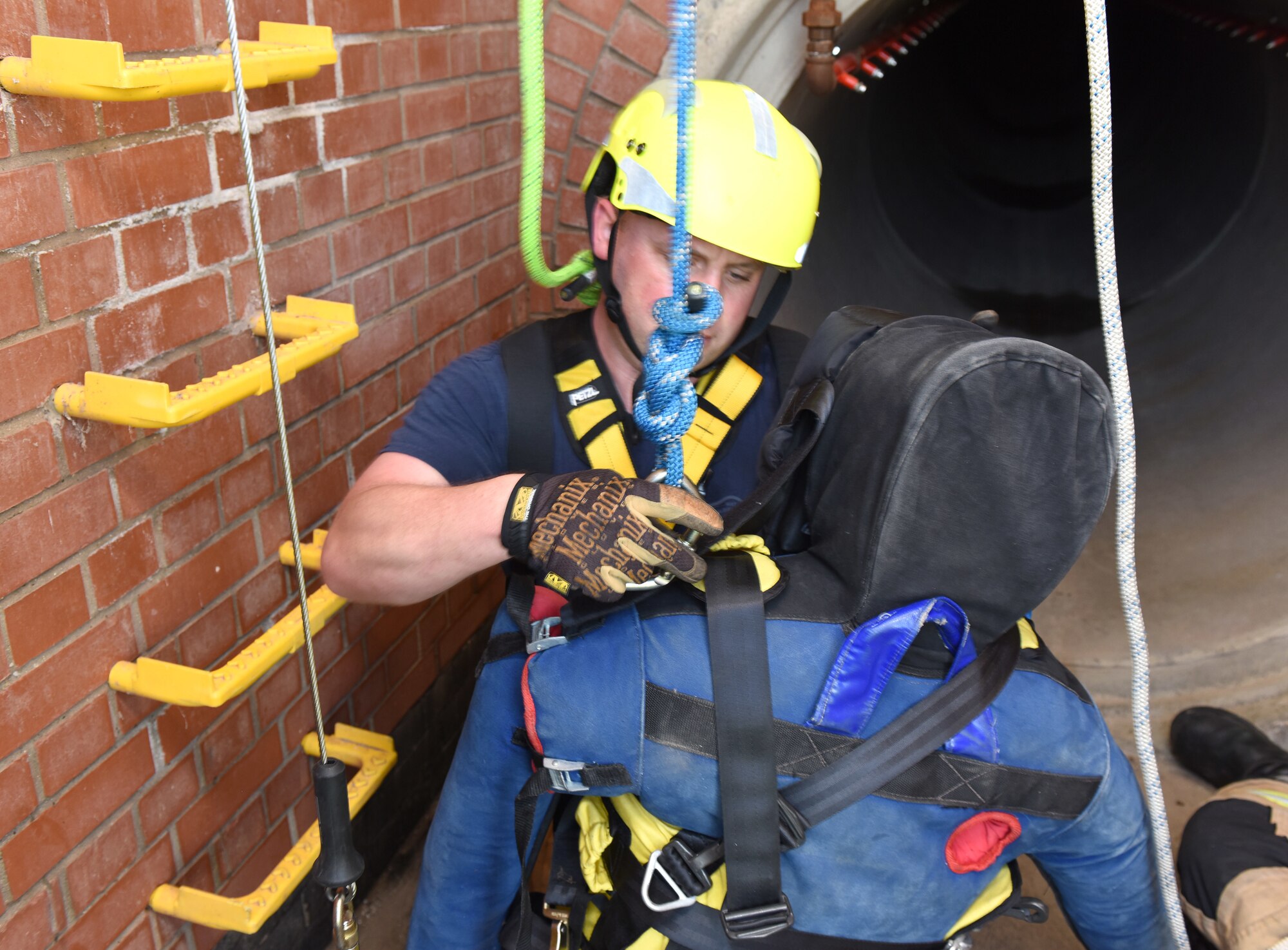 Firefighter Eddie Brant, 100th Civil Engineer Squadron Fire Department, fits an extraction harness onto a simulated victim during confined space training at Royal Air Force Mildenhall, England, April 14, 2022. The exercise scenario involved a teenager (simulated by the mannequin) who fell and was injured after climbing down into an underground facility. Another firefighter simulated also falling after slipping on a broken step while climbing down to rescue the victim, so other firefighters from his team had to complete the rescue. (U.S. Air Force photo by Karen Abeyasekere)