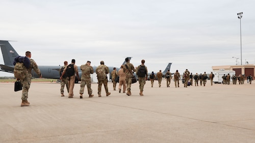 Large group of Airmen walking across the flight line after disembarking aircraft.