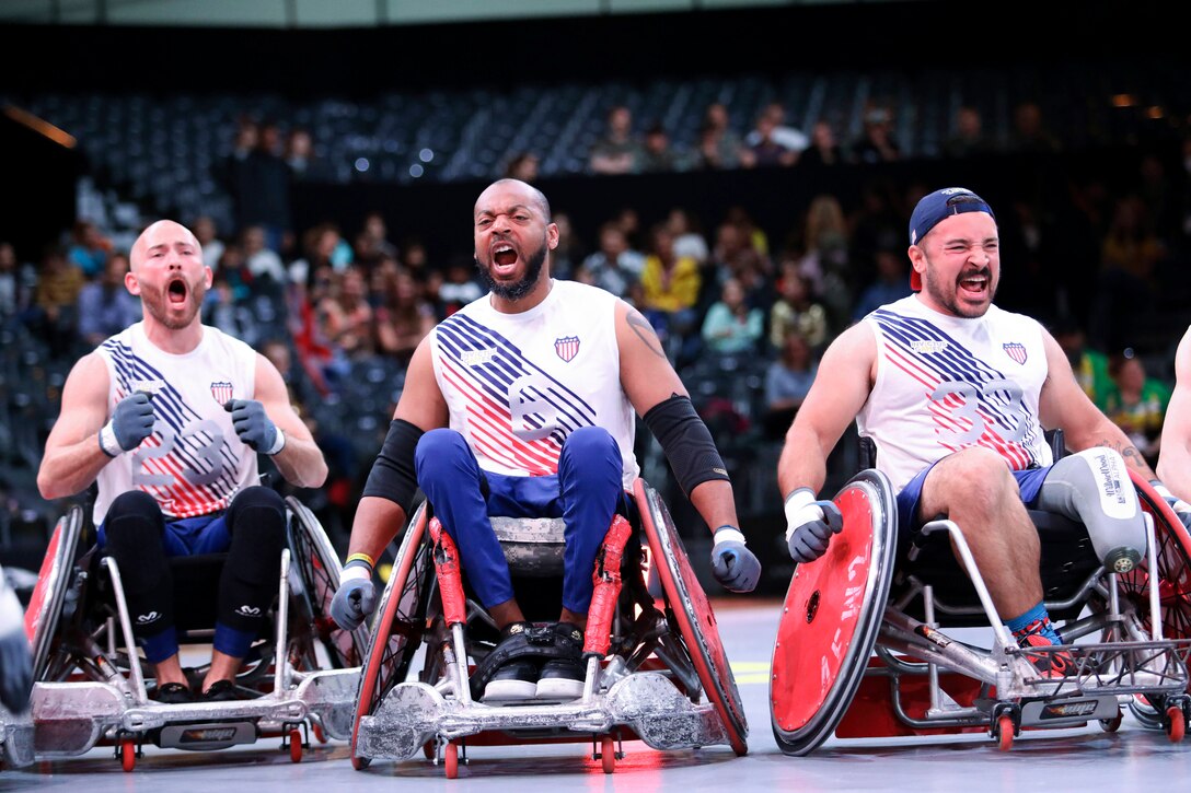 Three retired service members in wheelchairs cheer during a competition.
