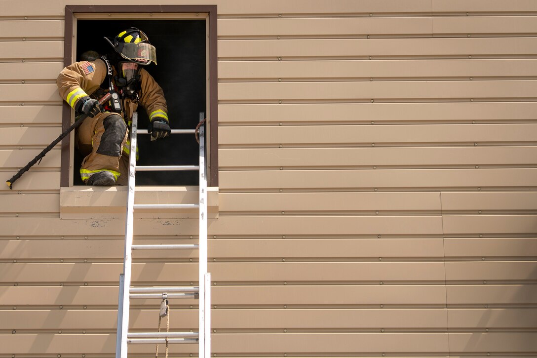 An airman climbs on a ladder out of a window during training.