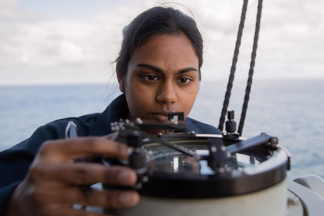 A sailor looks closely at a device.