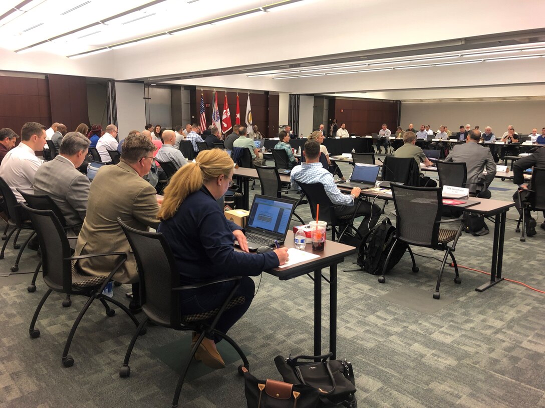 50 people in business attire with laptop computes in a conference room.