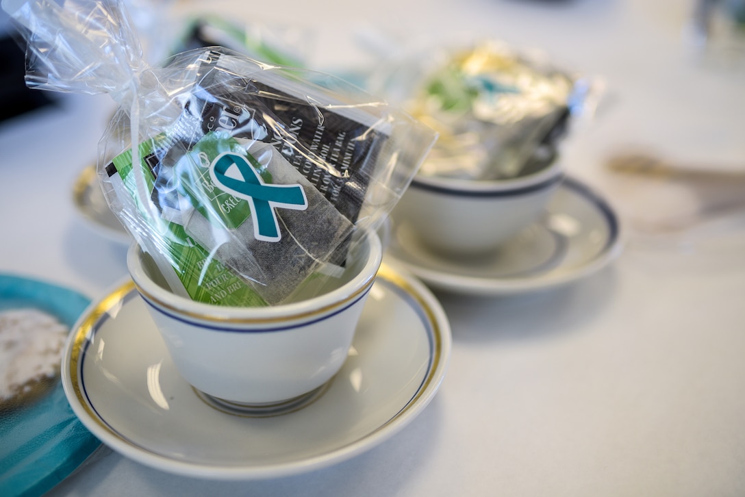 A teacup with a Sexual Assault Awareness ribbon and snacks sits on a white tableclothed table.