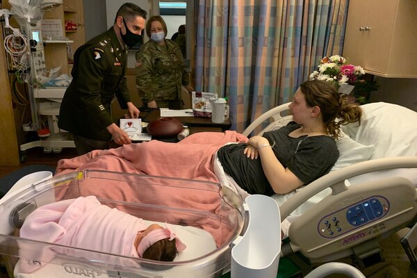 A man delivers a meal to a mother lying in bed with her baby next to her.
