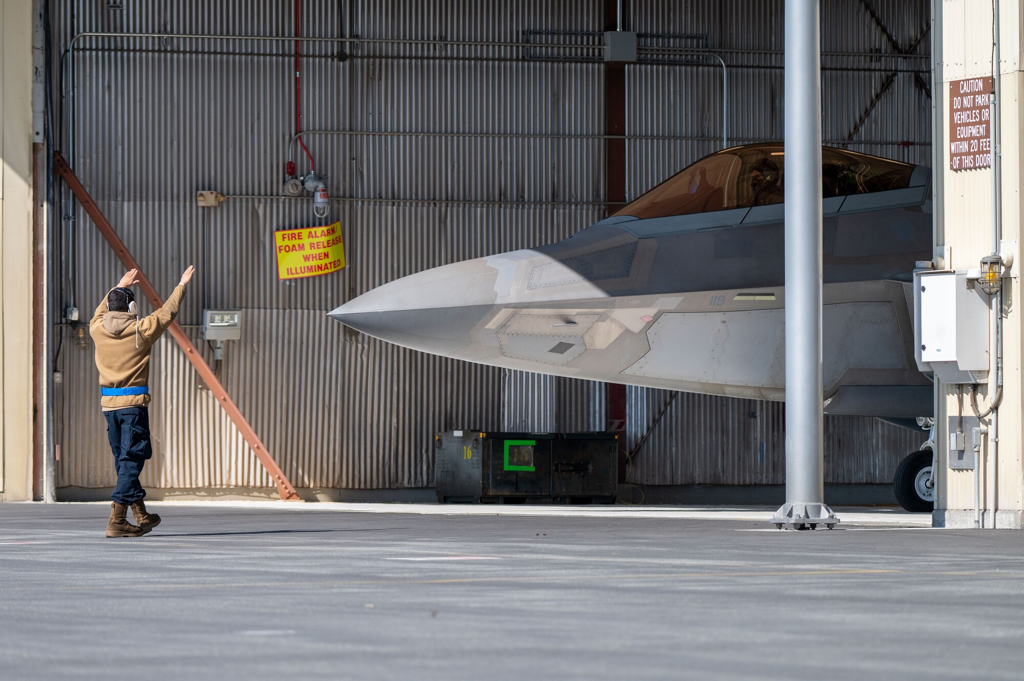 A photo of a crew chief marshaling an F-22 Raptor out of its hangar.