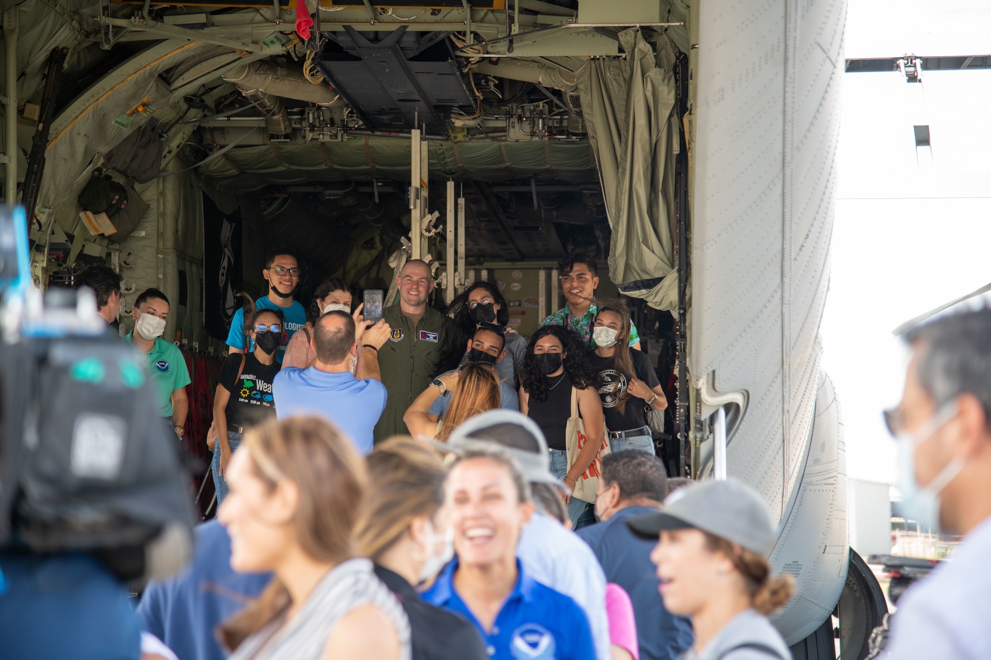 Crowd of people in foreground. Manganaro poses with students on the ramp of an aircrat.