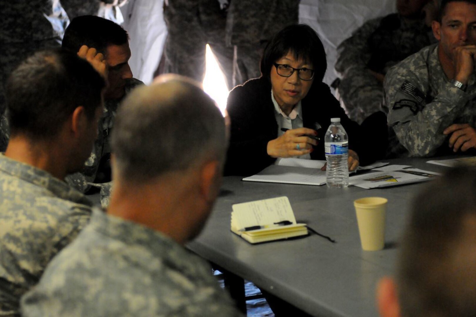 A woman sits at a table surrounded by men in uniform.