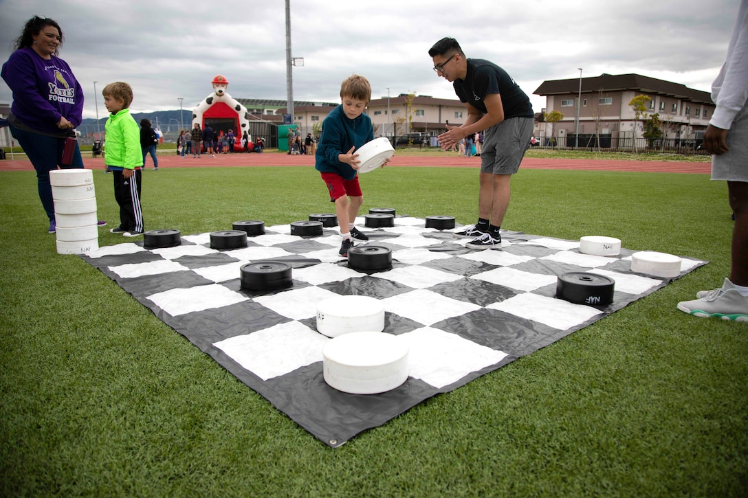 A child plays checkers  on a large checkerboard laid out on the grass.