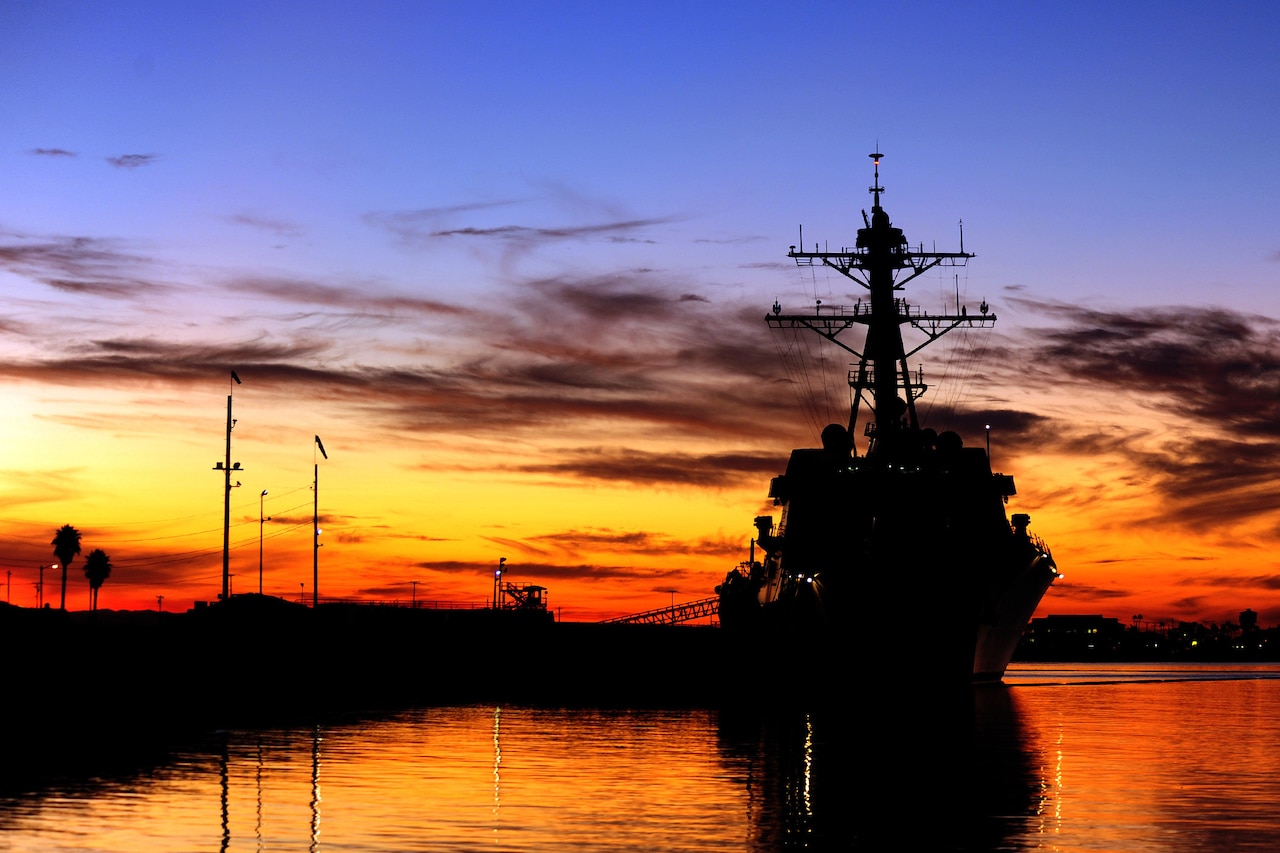 A ship is docked and backlit by orange and blue light at dusk.