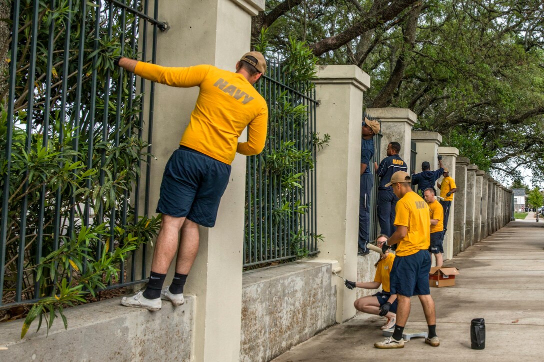 Sailors paint a stretch of wall lining a city sidewalk.