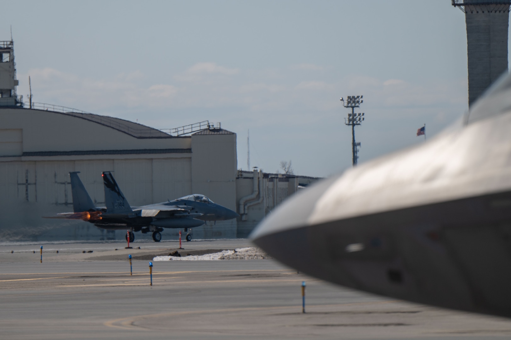 A photo of an F-15 Eagle taking off next to the nose of an F-22 Raptor.