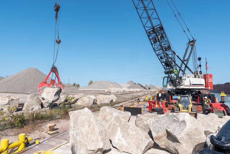 A crane on a barge hoists a large stone into place on a breakwater.