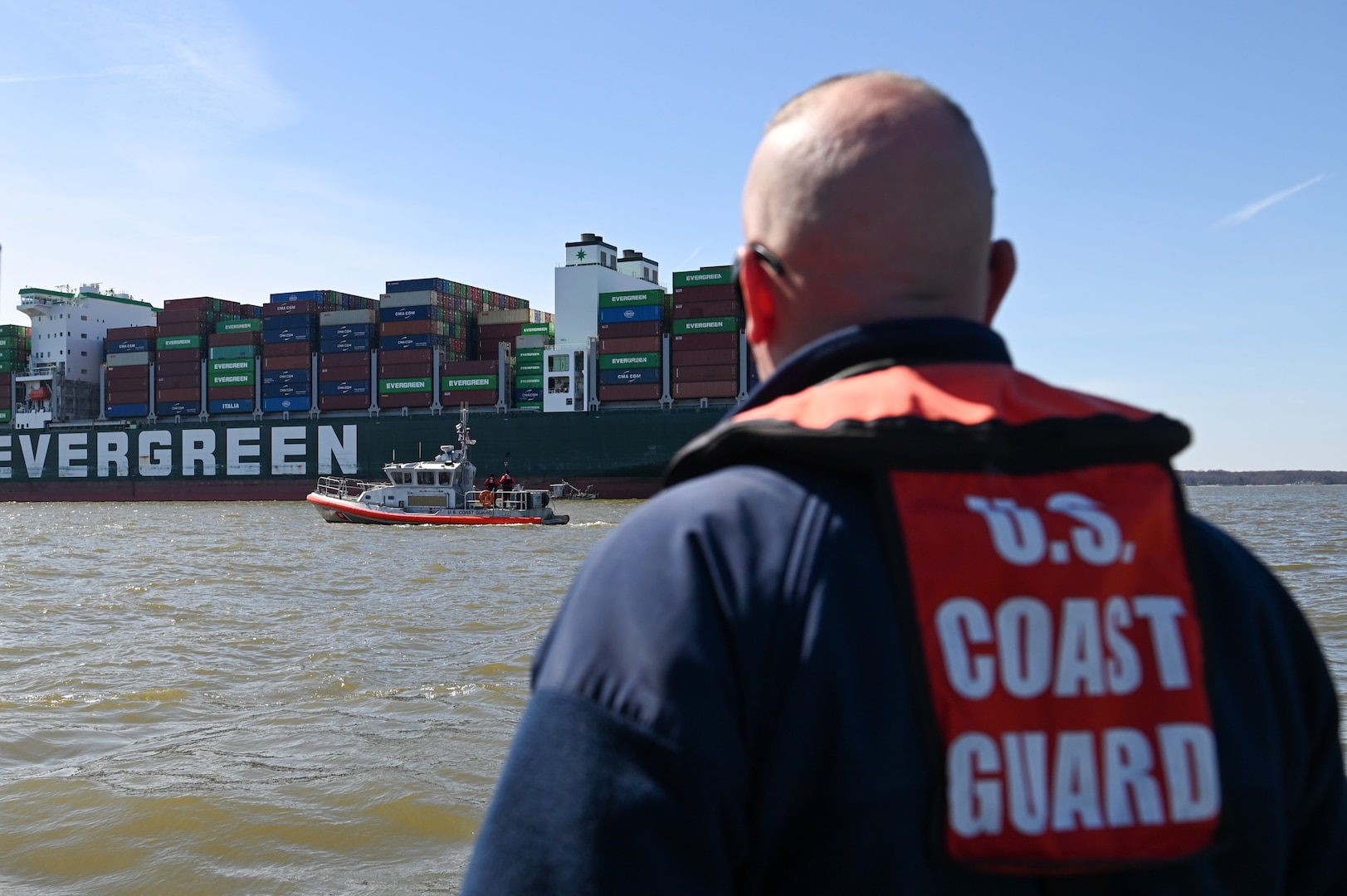 Coast Guard member monitors container ship from the deck of a response boat