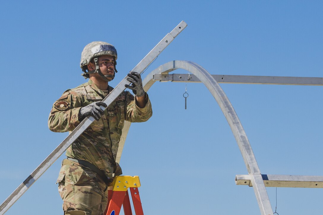 A U.S. Air Force Airman attaches a beam to aid in securing the frame of an Alaskan Small Shelter System at the Silver Flag exercise site on Tyndall Air Force Base, Florida, March 31, 2022. The primary focus of Silver Flag is to teach Airmen from the civil engineer, force support, and vehicle maintenance squadrons essential skills to complete operations outside of their primary duties. (U.S. Air National Guard photo by Senior Airman Jana Somero)