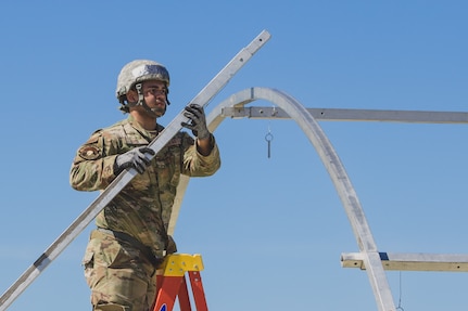 A U.S. Air Force Airman attaches a beam to aid in securing the frame of an Alaskan Small Shelter System at the Silver Flag exercise site on Tyndall Air Force Base, Florida, March 31, 2022. The primary focus of Silver Flag is to teach Airmen from the civil engineer, force support, and vehicle maintenance squadrons essential skills to complete operations outside of their primary duties. (U.S. Air National Guard photo by Senior Airman Jana Somero)