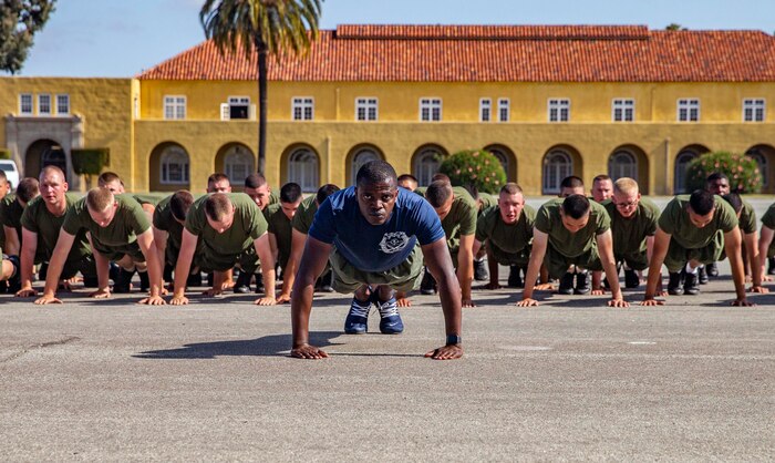 U.S. Marine Corps Staff Sgt. Anthony Brown with Mike Company, 3rd Recruit Training Battalion, executes push-ups with his platoon during a motivational run at Marine Corps Recruit Depot San Diego, April 21, 2022. New Marines conducted warm-up exercises in front of their friends and family before the run. (U.S. Marine Corps photo by Cpl. Grace J. Kindred)