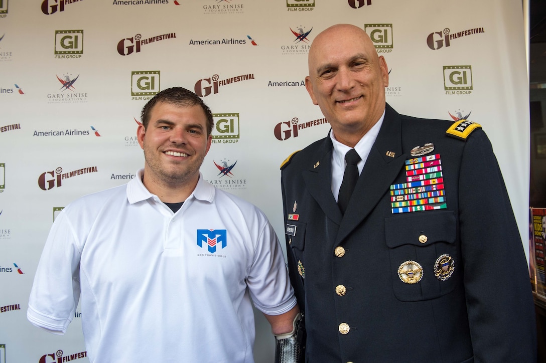Two men, one in civilian clothes the other in uniform, stand in front of a backdrop noting that they are at the GI Film Festival.