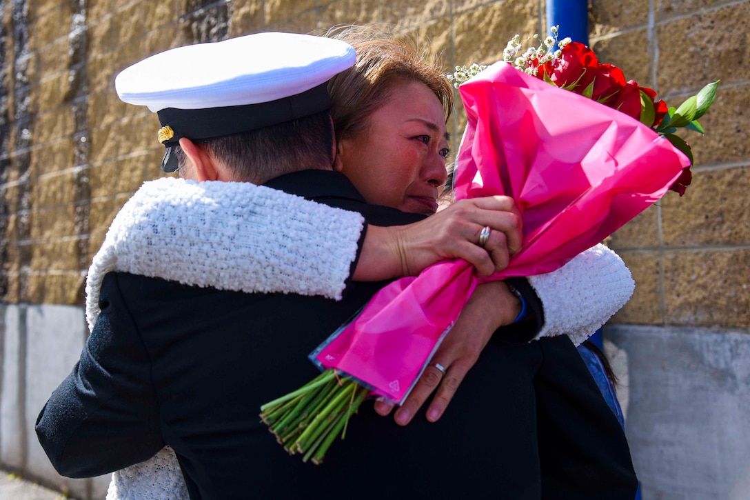 A woman hugs a sailor while holding flowers.