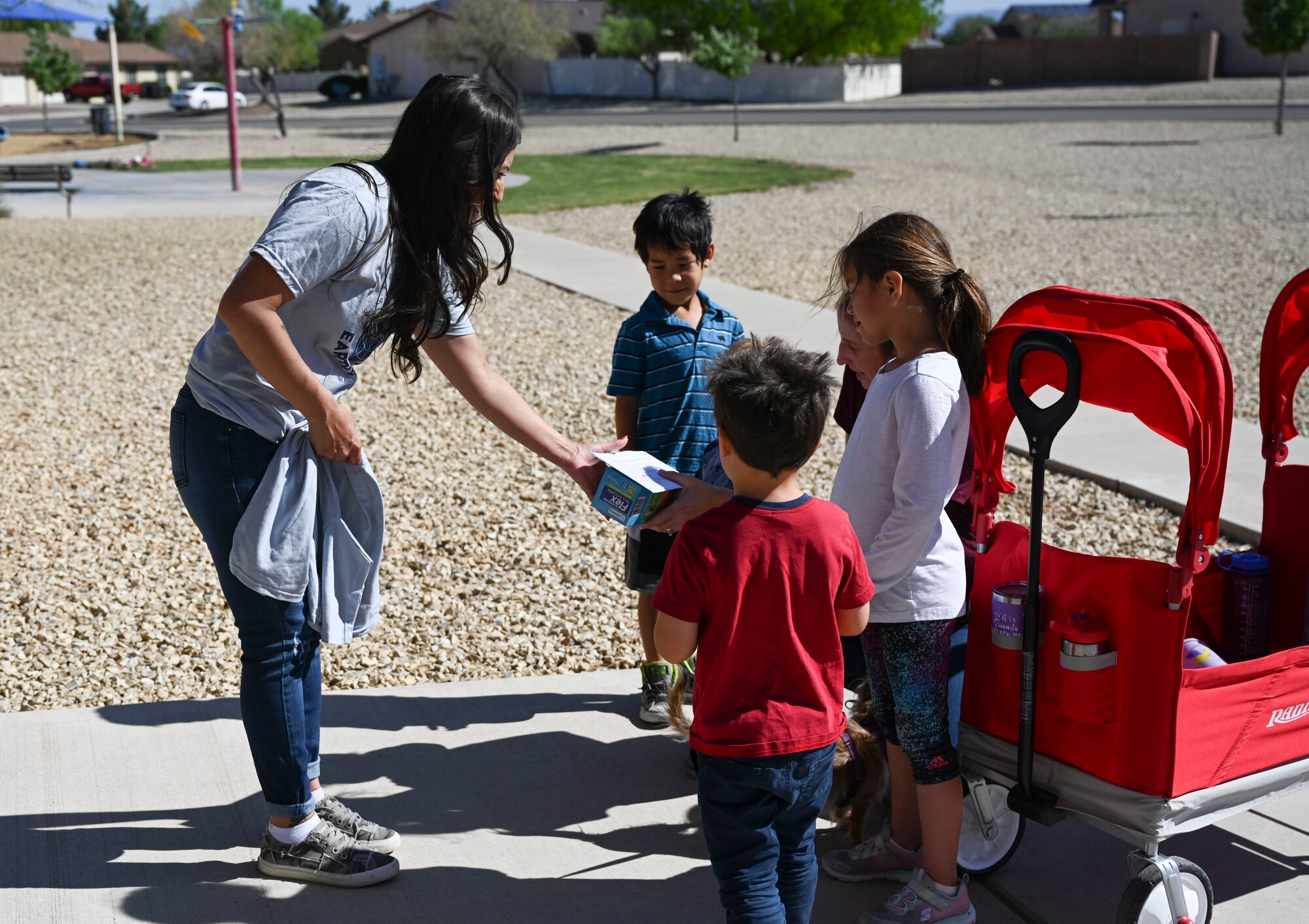 Althea Strong, Soaring Heights Communities property manager, hands a group of children some trash bags and t-shirts at an Earth Day extravaganza on Holloman Air Force Base, New Mexico, April 21, 2022. This event allowed Soaring Heights Communities residents  to volunteer to clean up their respective neighborhoods and take home their own plants. (U.S. Air Force photo by Airman 1st Class Antonio Salfran)