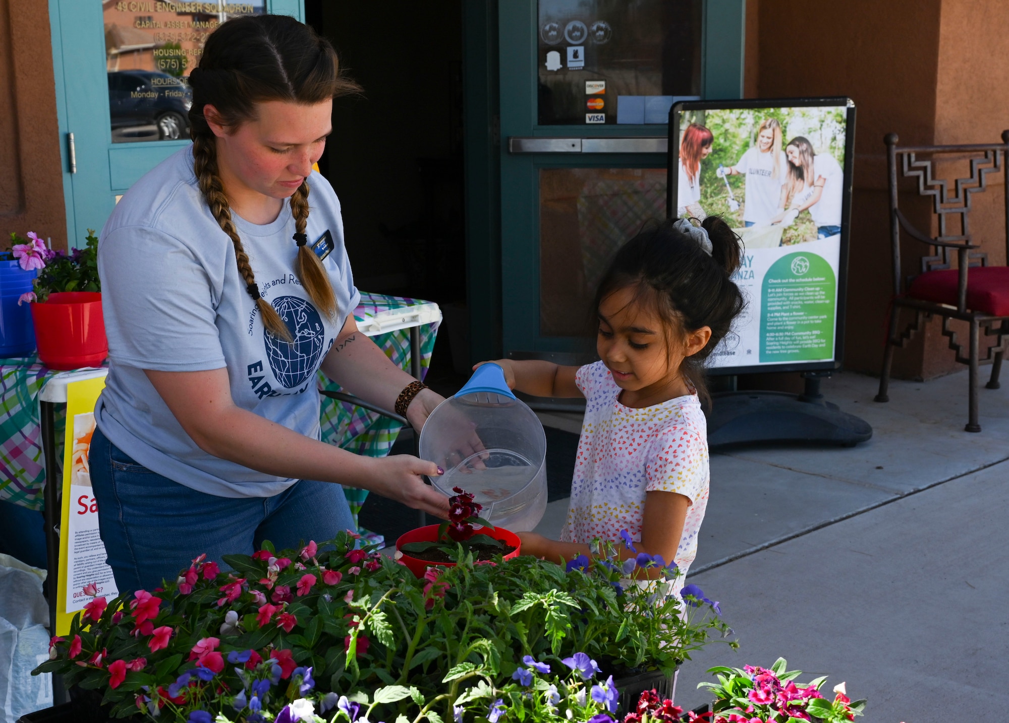 A Soaring Heights Communities team member helps a child water plants during an Earth Day extravaganza at the Soaring Heights Communities leasing office, on Holloman Air Force Base, New Mexico, April 21, 2022. Part of the extravaganza involved a two-hour block for Holloman families to plant and take home fresh flowers. (U.S. Air Force photo by Airman 1st Class)