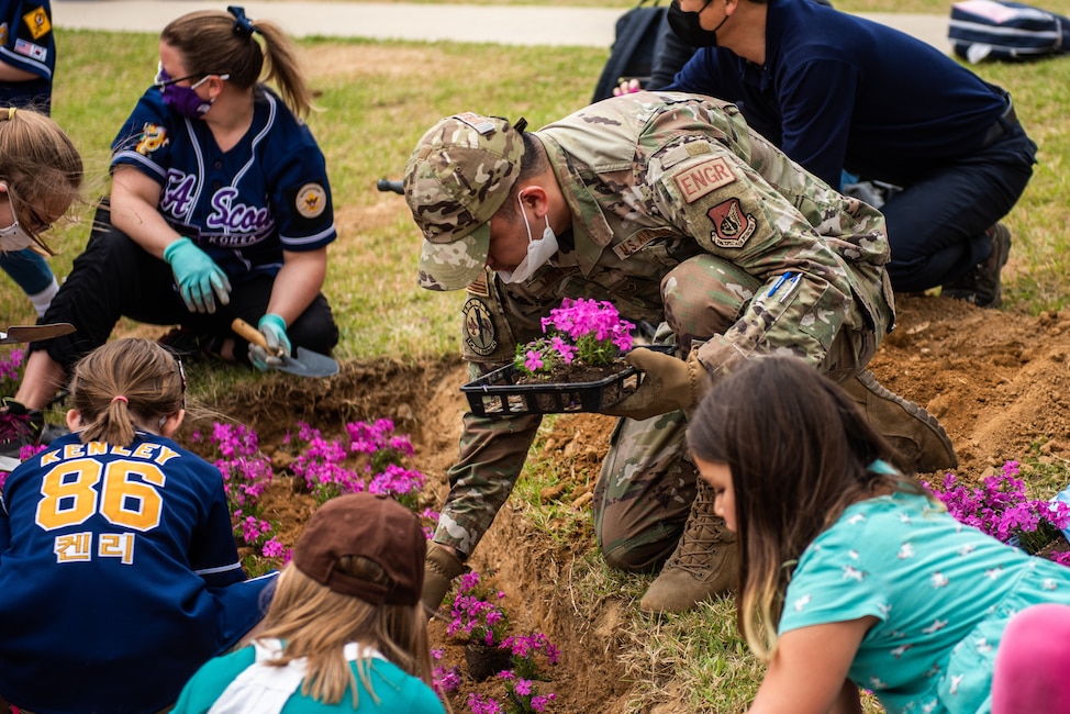 Senior Airman Julien Miranda, 51st Civil Engineer Squadron engineering technician, assists students planting flowers in front of Osan Elementary School, 22 April, 2022 at Osan Air Base, Republic of Korea.