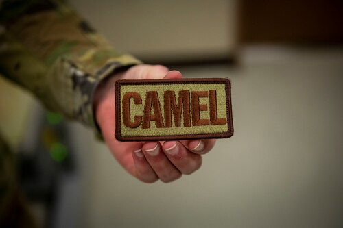 Military member in uniform holds a patch reading "Camel".