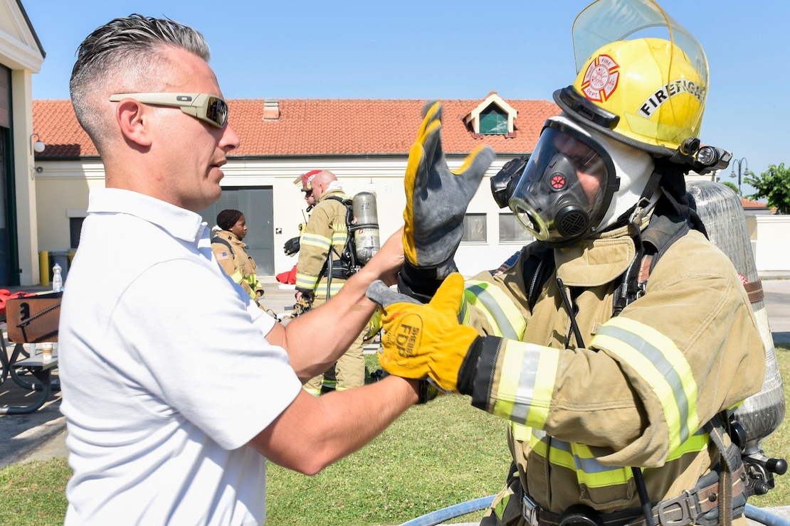 Naval Support Activity (NSA) Naples Fire Chief Nicholas Panzica, left, performs a safety check on the glove of  Marco Annunziata, a local national firefighter at NSA Naples, during a live fire training exercise on board NSA Naples’ Support Site, June 26, 2020.