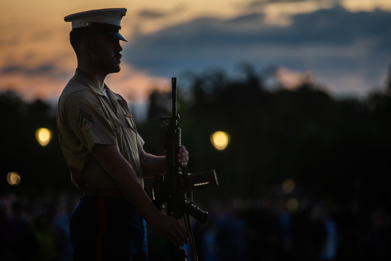 A Marine presents arms during a ceremony as shown in silhouette.