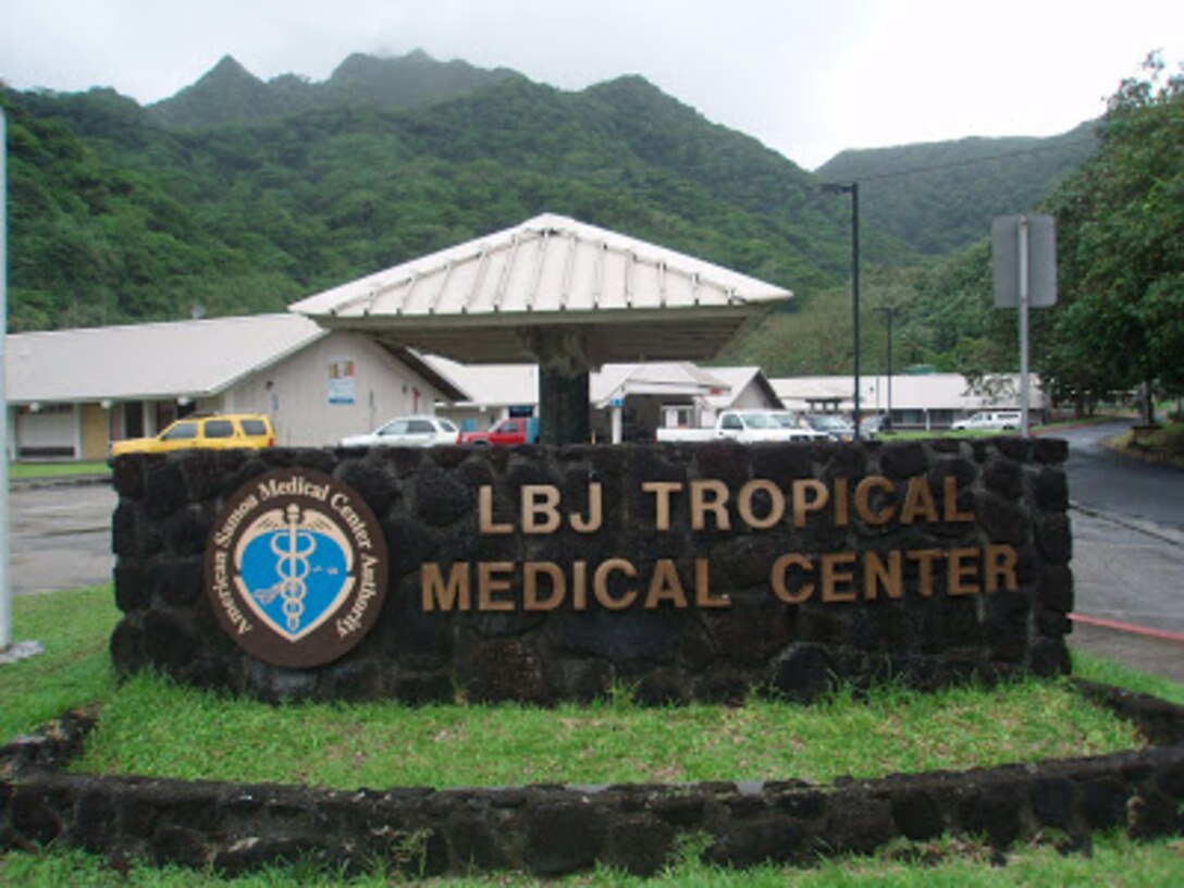 A sign reading "LBJ Tropical Medical Center" on a stone wall sits in the foreground of a photo of a building.