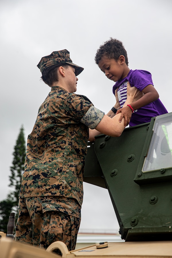A U.S. Marine helps a child out of a Joint Light Tactical Vehicle during the Headquarters and Support Battalion Family Day event on Camp Foster, Okinawa, Japan, on April 22, 2022. Family Day allowed service members to engage in activities with their children, allowing them to view military vehicles, participate in a mock combat fitness test, and learn professional training from the Marine Corps Martial Arts Program and the Marksmanship Training Unit. (U.S. Marine Corps photo by Cpl. Alex Fairchild)