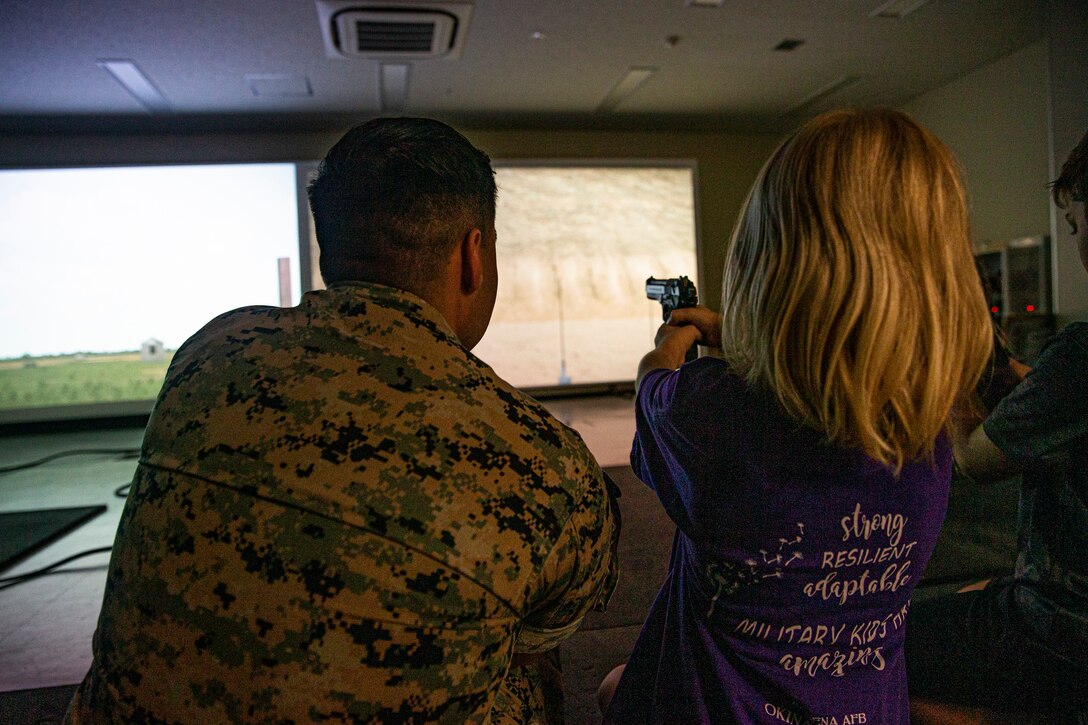 Service members and their families practice pistol marksmanship using the Indoor Simulated Marksmanship Trainer during the Headquarters and Support Battalion Family Day event on Camp Foster, Okinawa, Japan, on April 22, 2022. Family Day allowed service members to engage in activities with their children, allowing them to view military vehicles, participate in a mock combat fitness test, and learn professional training from the Marine Corps Martial Arts Program and the Marksmanship Training Unit. (U.S. Marine Corps photo by Cpl. Alex Fairchild)