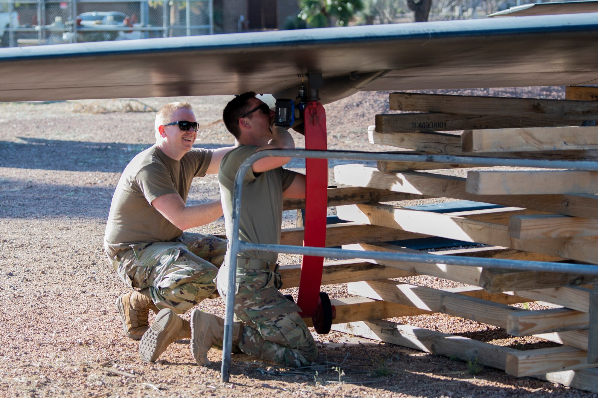 Two Airmen are under an aircraft wing working together to detach it from the aircraft body.