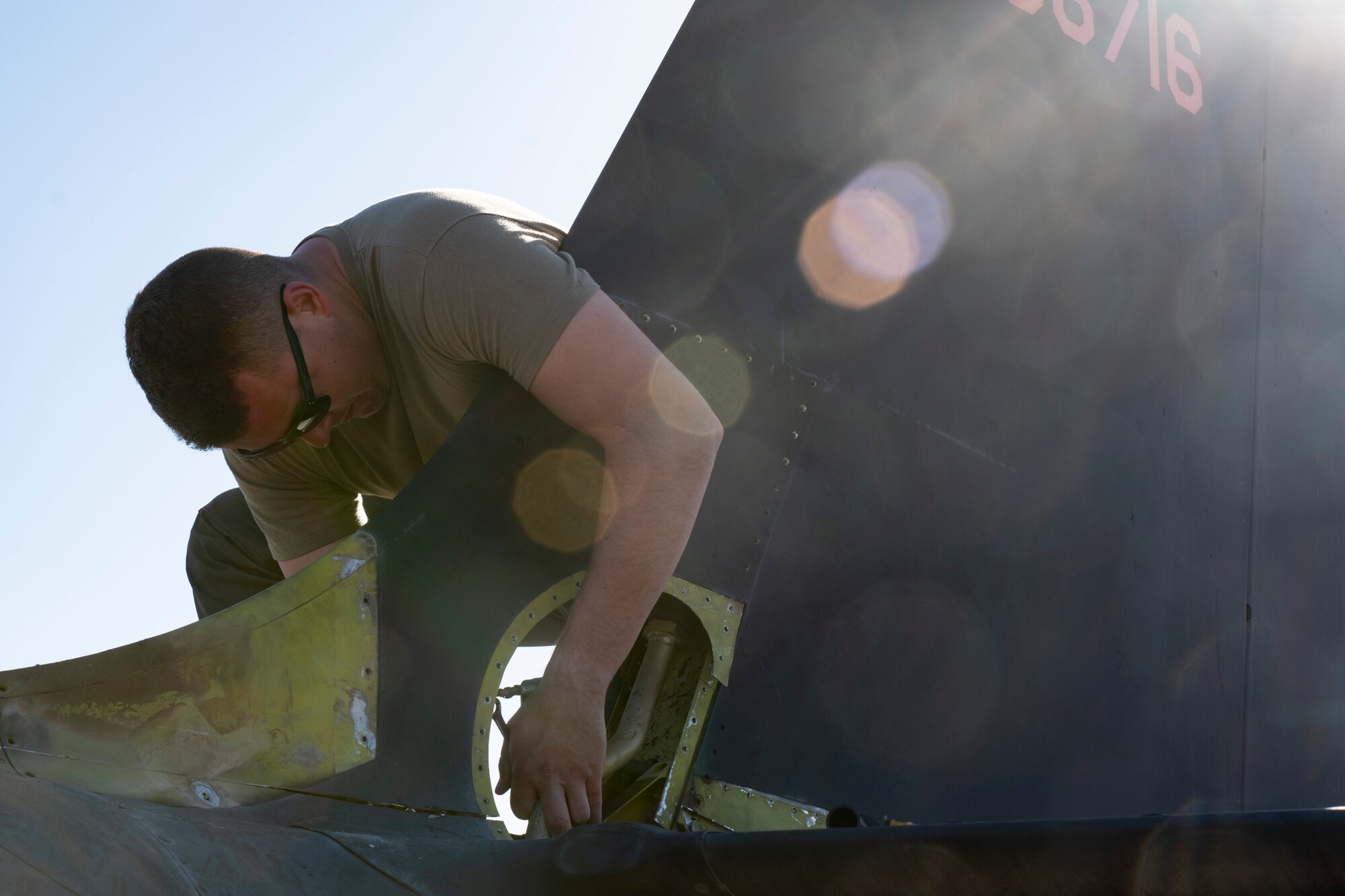 An Airmen is leaning over the tail of an aircraft, working to detach it from the body of the aircraft.