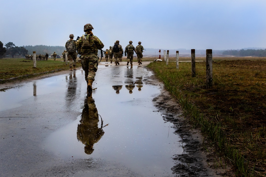 Soldiers walk up the road while carrying their backpacks.