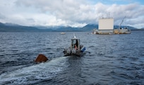 A boat carrying a buoy heads toward one of SEAFAC’s suspension barges before conducting an acoustic trial in the Behm Canal near Ketchikan, Alaska.