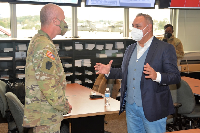 A man wearing a mask speaks to another man in military uniform.