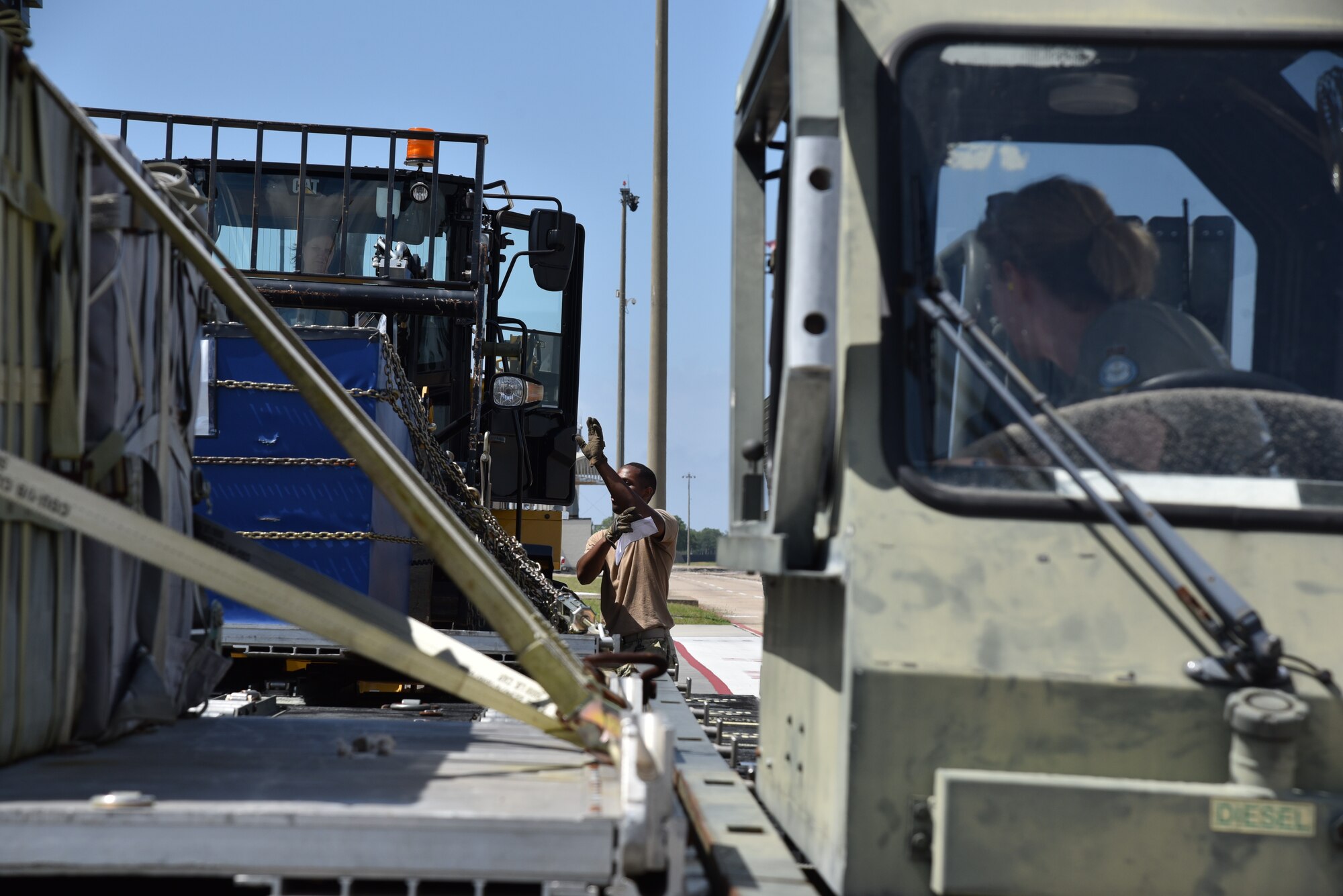 British Royal Air Force Reserve member watches from the seat of the K-loader, while U.S. Air Force Reserve member marshals the driver of the all terrain 10K forklift to put the pallet on the K-Loader.