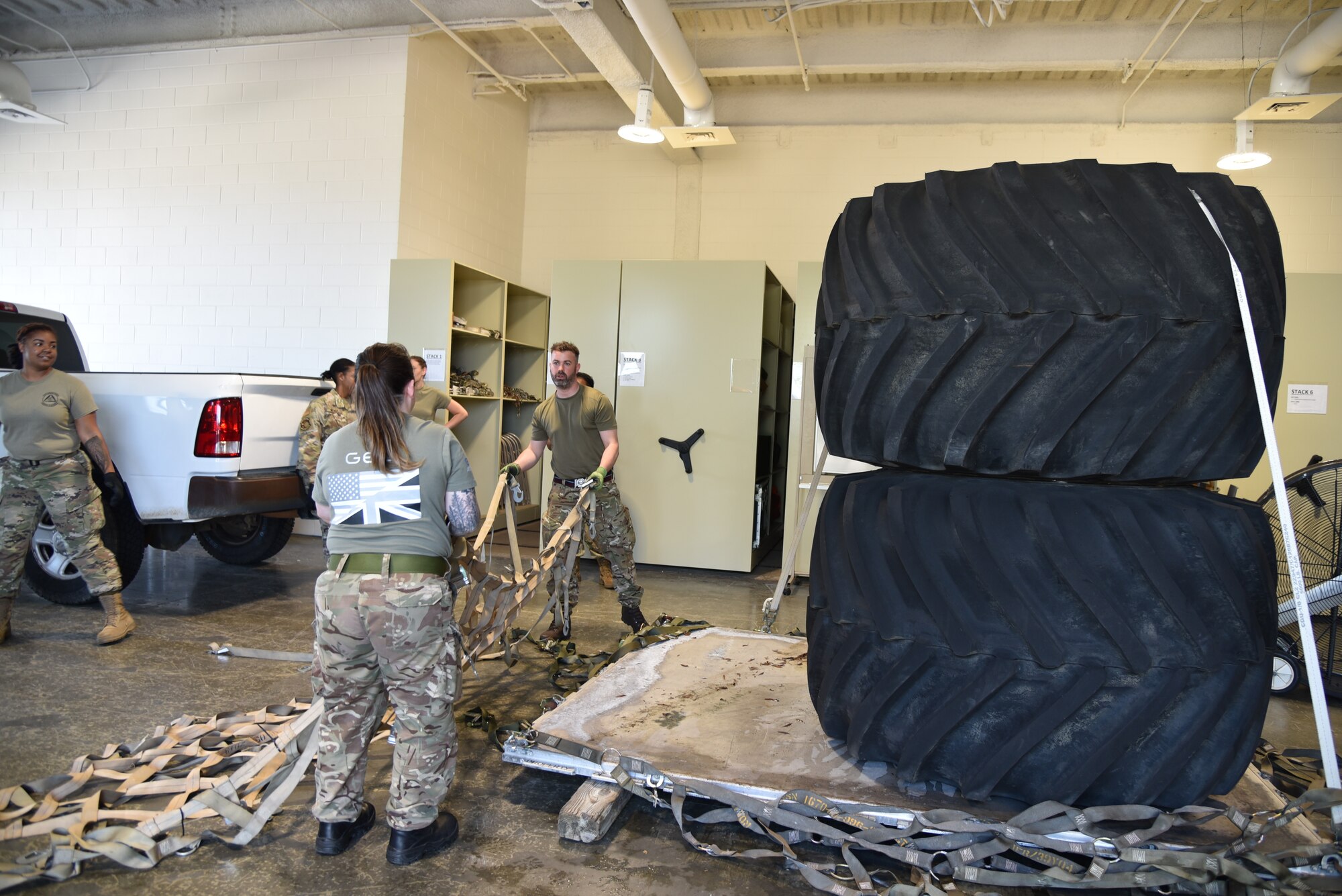 British Royal Air Forces members throw cargo net over top of tires stacked on pallet for training.