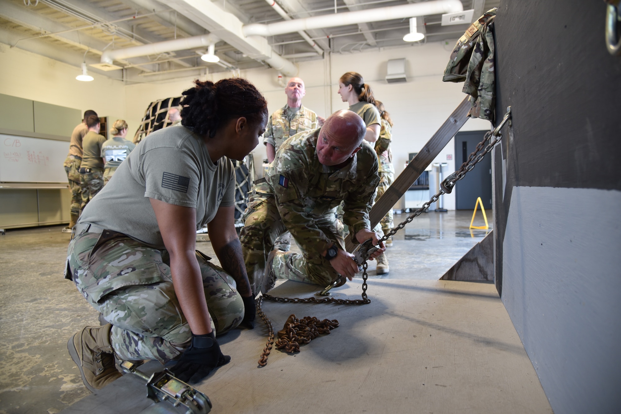Female Air Force Reserve Airman talking the British Royal Air Force Warrant Officer through how the US tie down chain equipment works.