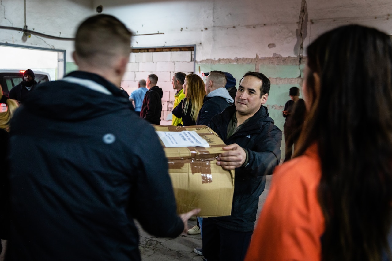 A man passes a box to another man in a room full of people.