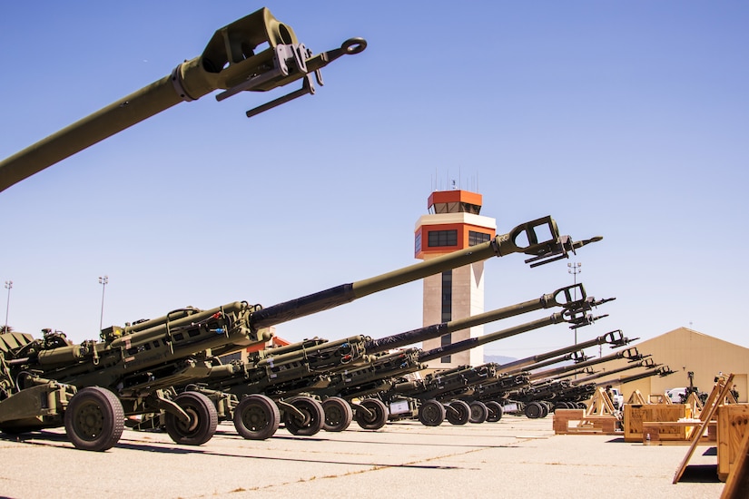 Several howitzer artillery guns are lined in an airfield.