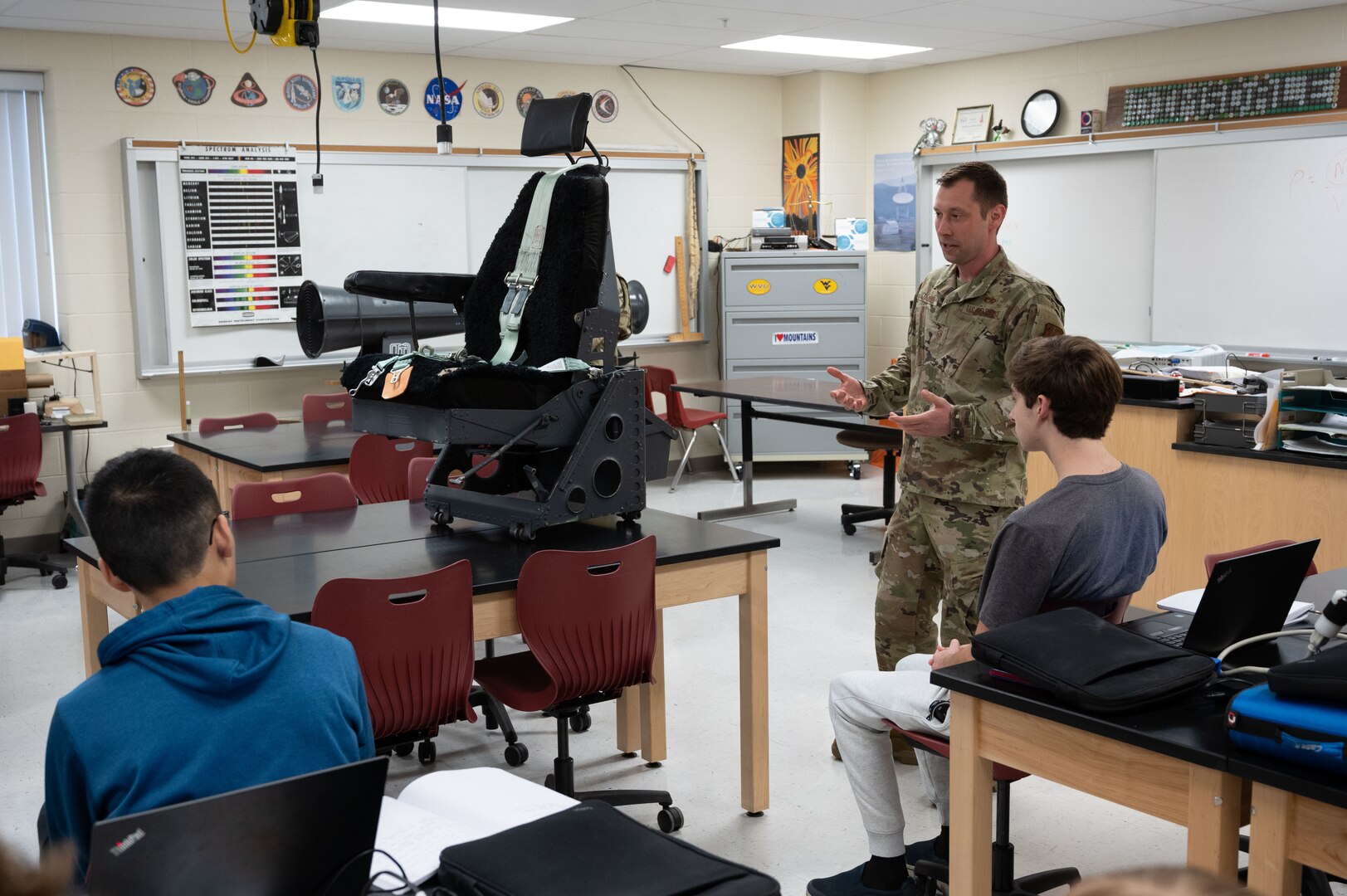 Master Sgt. Jeffery Jackson, a First Sergeant, assigned to the 130th Maintenance Squadron explains the function of a C-130 E model aircraft seat to a group of High School students at Hurricane Hight School in Hurricane, West Virginia, April 26, 2022. The Aircraft seat was donated to the aerospace engineering students as an example of an aircraft seat designed for extended flight hours. (U.S. Air National Guard photo by Senior Master Sgt. Eugene Crist)