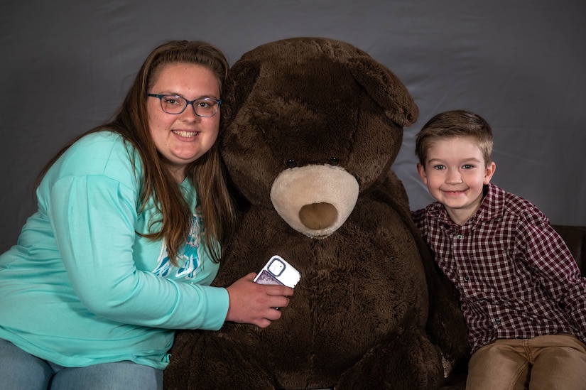 Two people lean on a large stuffed bear.