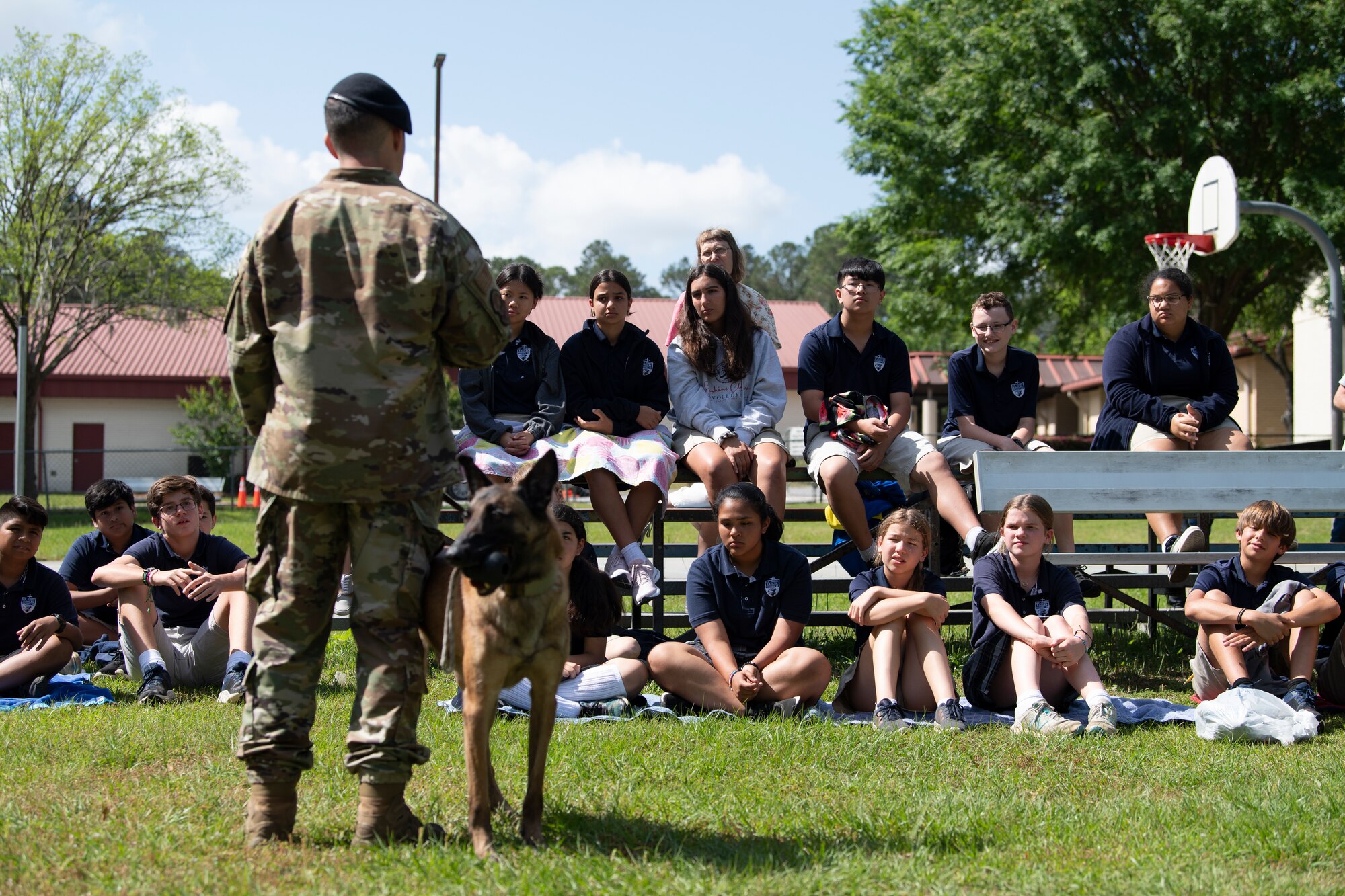 A photo of a man standing in front of a group of children holding his dog on a leash.