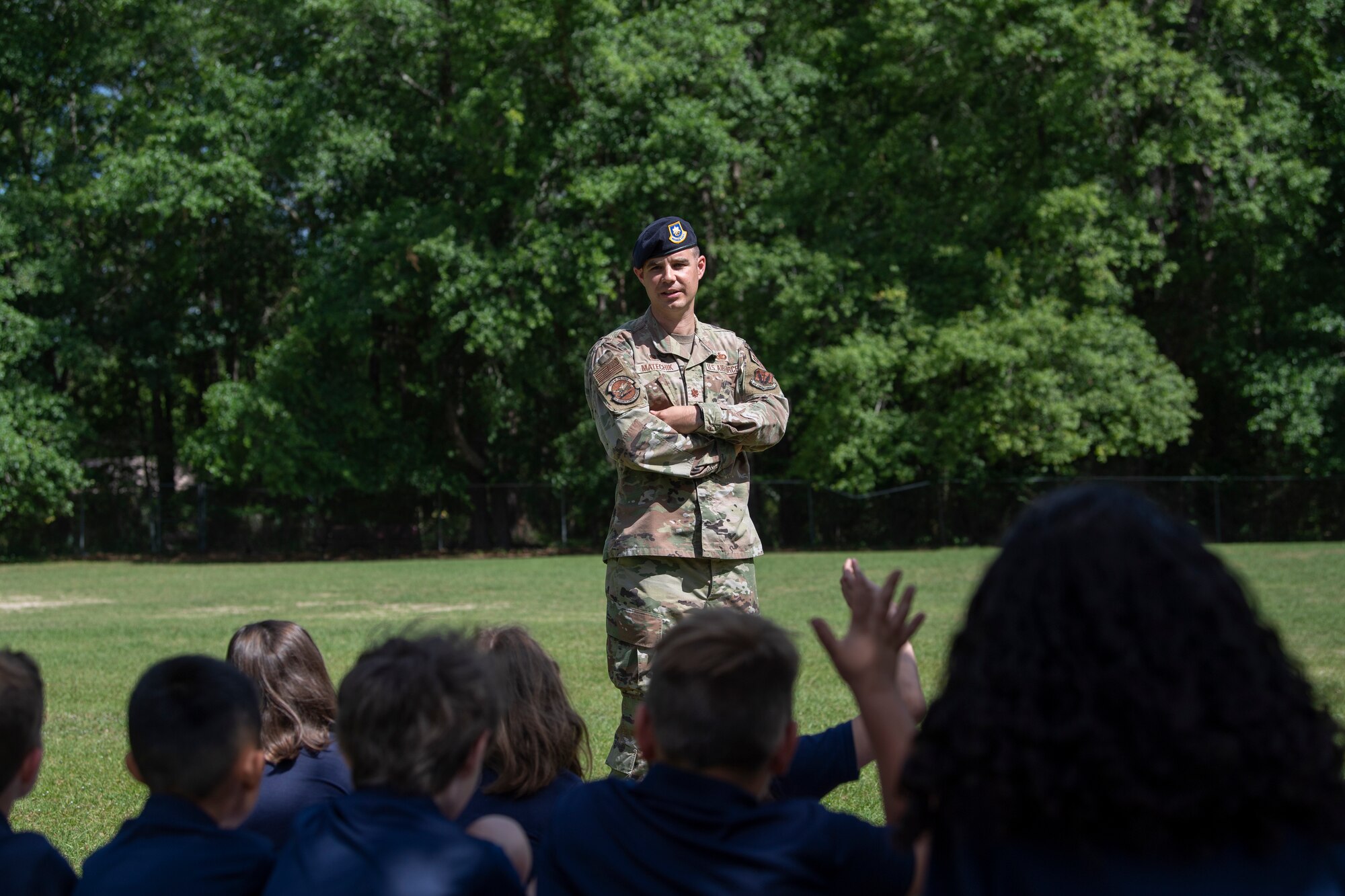 A photo of a man standing in front of a crowd of kids with his arms crossed.