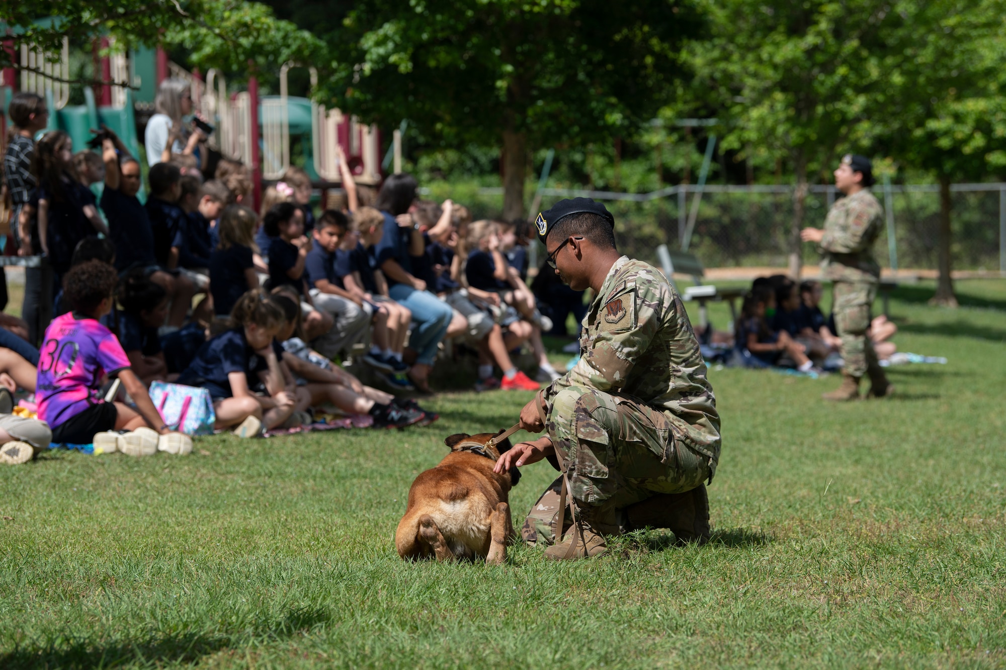 A photo of a man crouching down next to his dog in the grass.