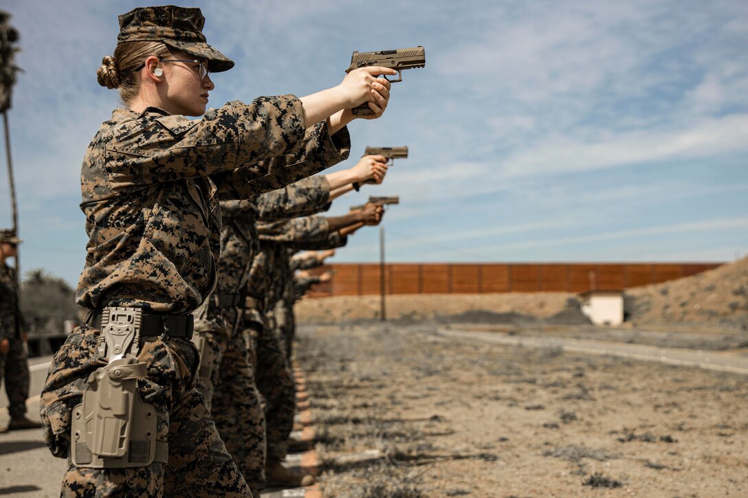 Marines standing in a line aim weapons.